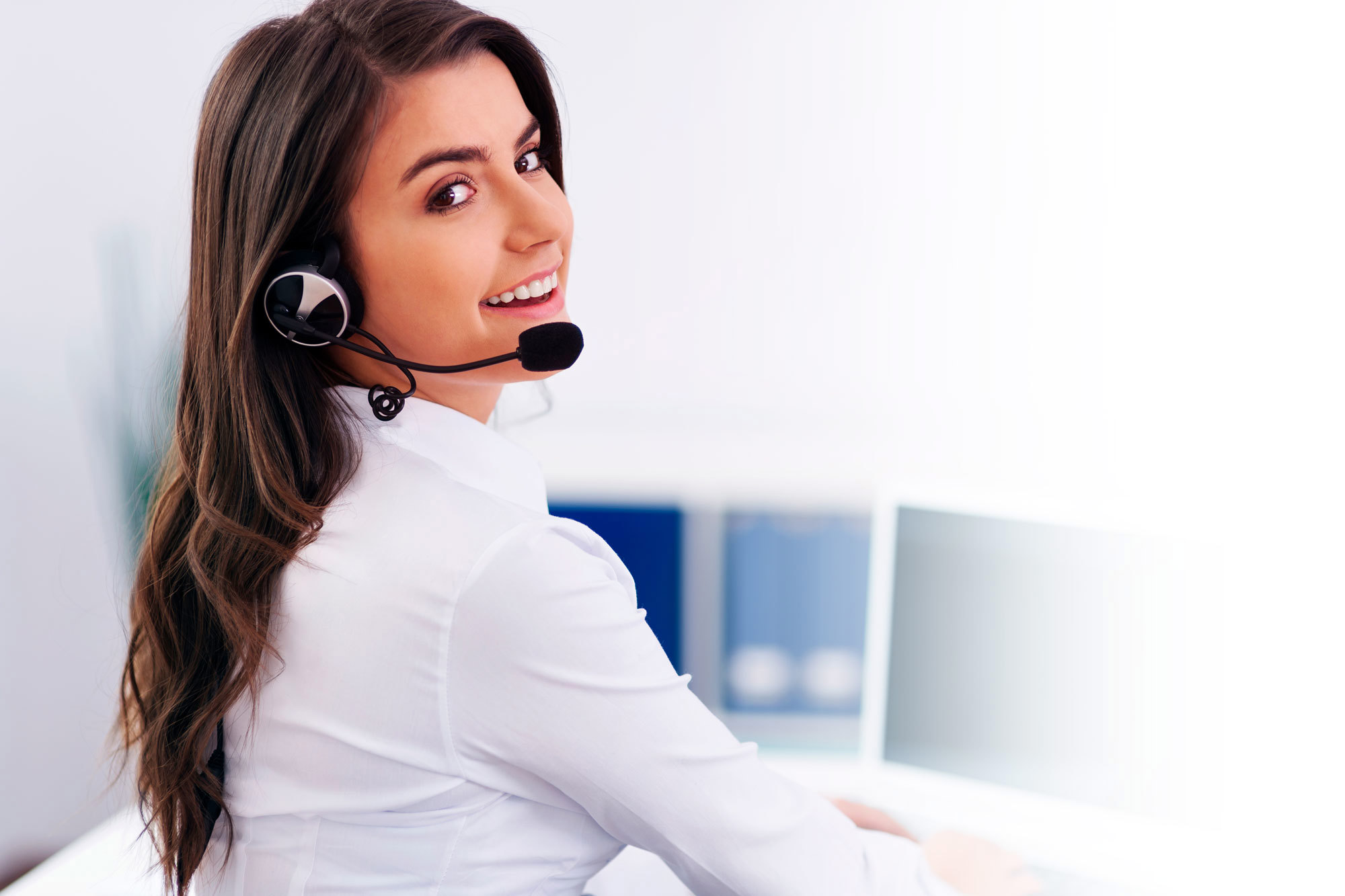 Smiling woman with headset working at a computer, providing customer support.