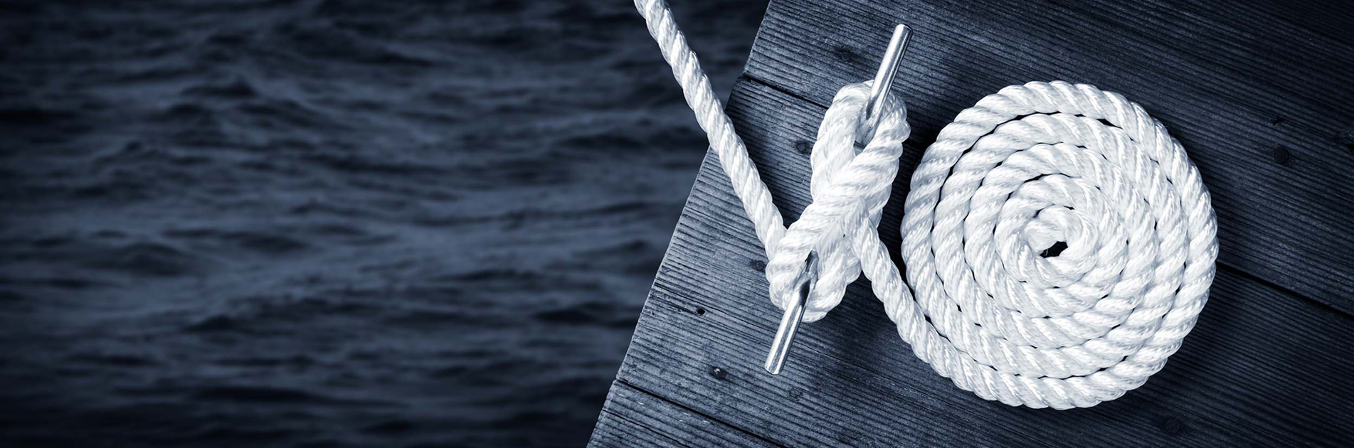 Coiled rope secured on a wooden dock with ocean in the background.